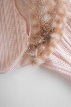 Close-up of a pink knitted garment with fur trim on a light background